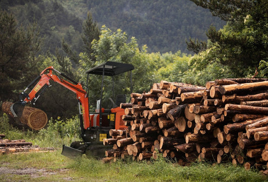 a small excavator removing piles of tree logs